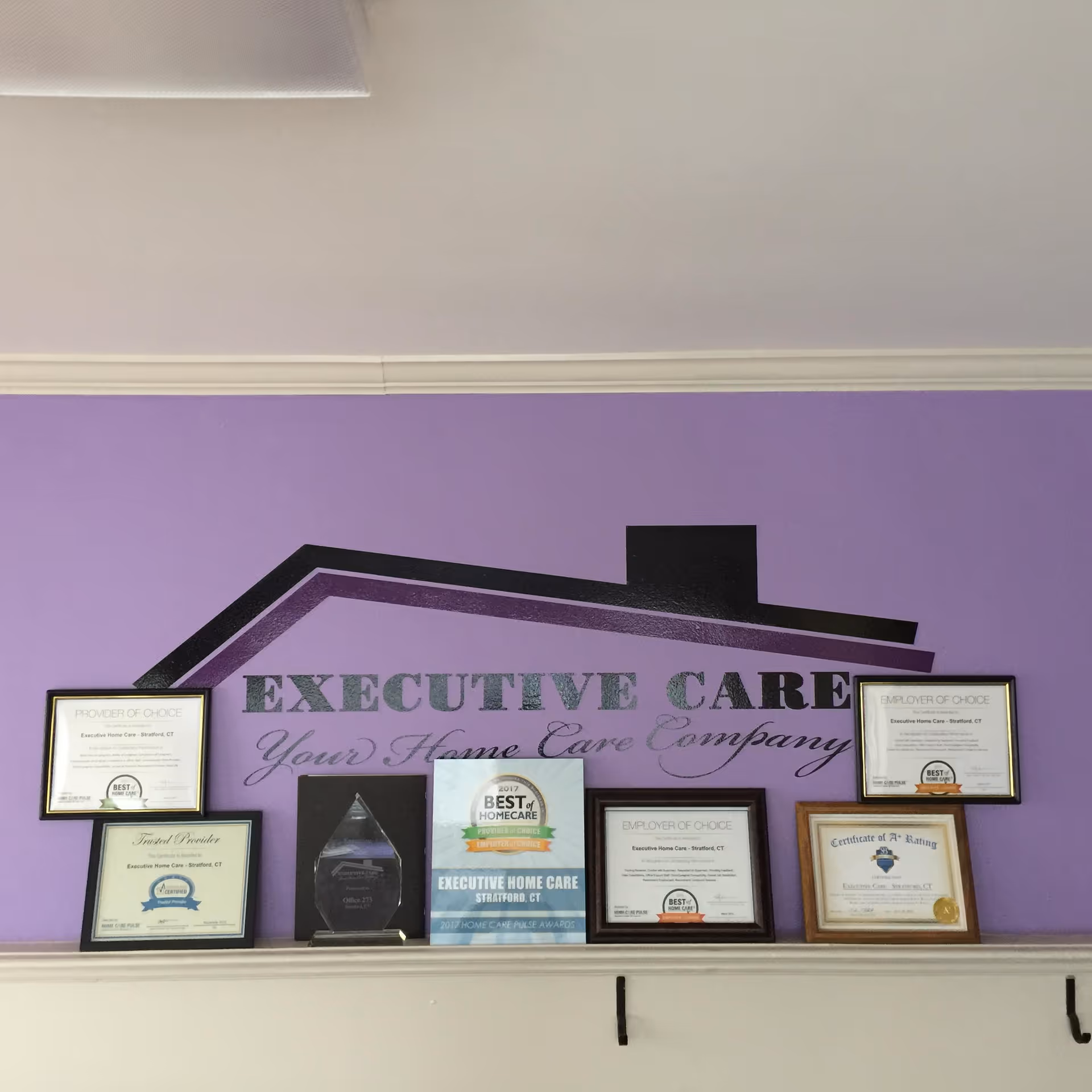 Interior with purple wall, framed awards, and Executive Home Care logo.