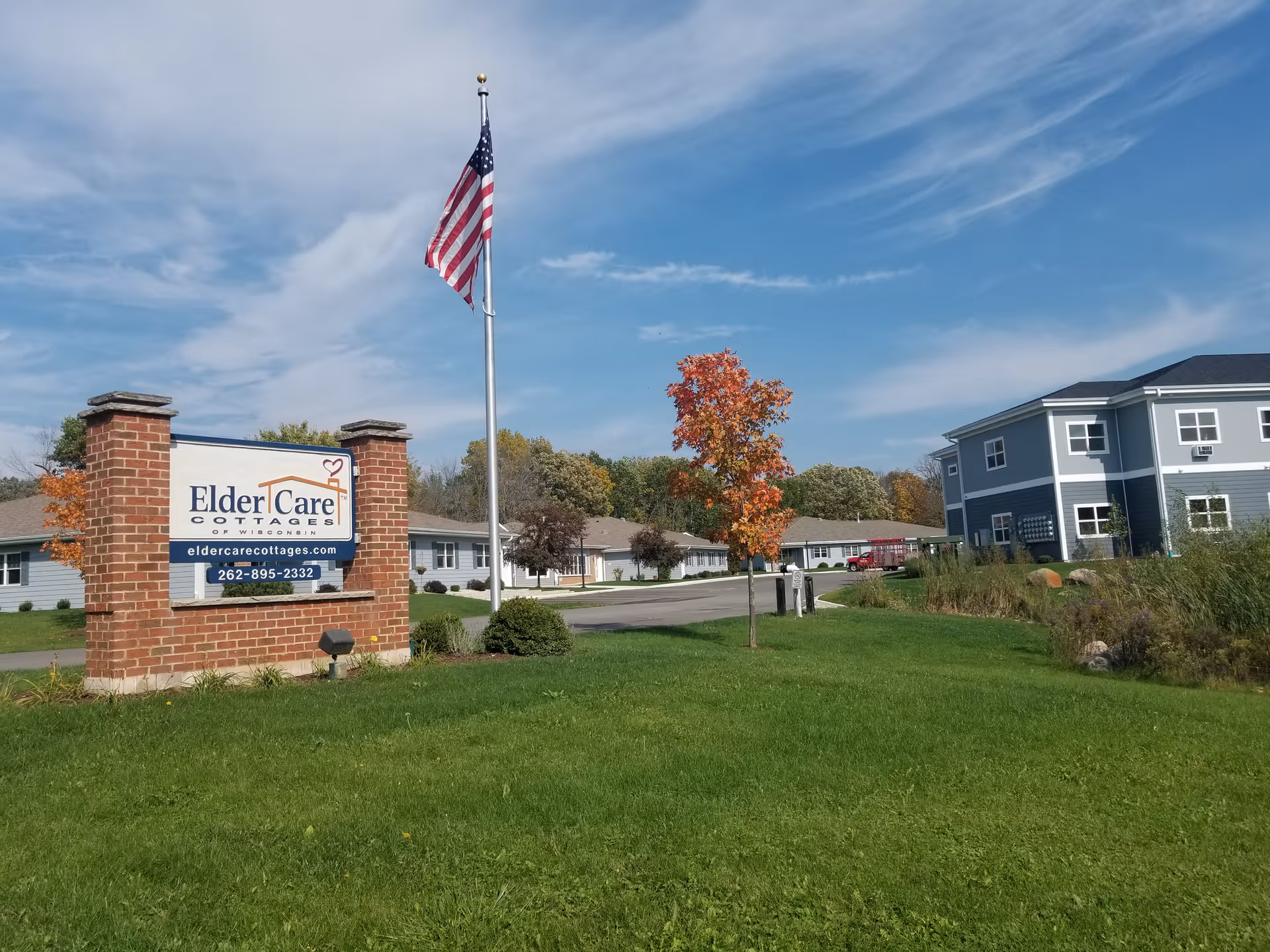 Exterior view of a senior care campus with a brick sign, flagpole, and two buildings.