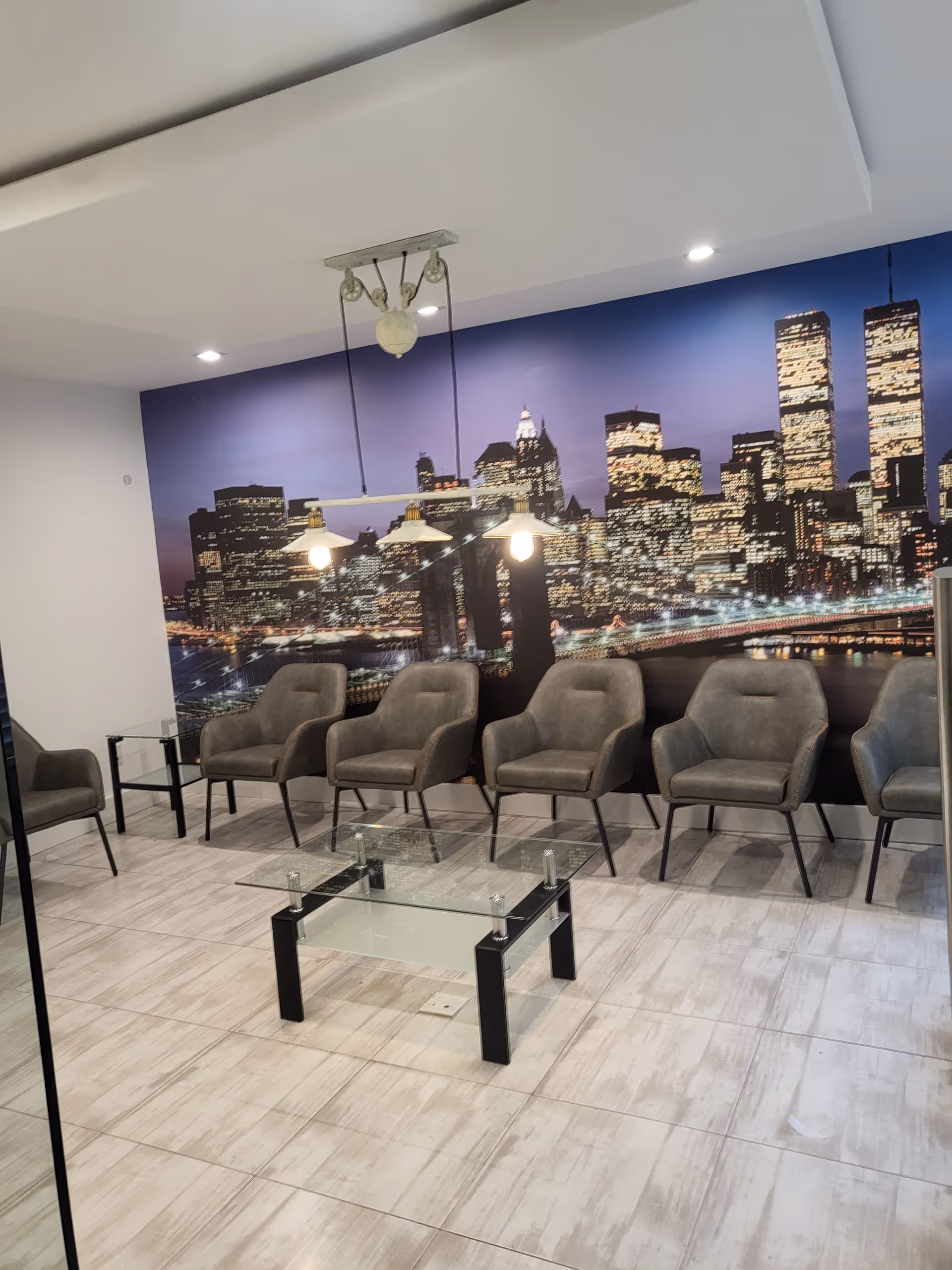 Row of gray chairs along a wall with a city skyline mural in a lobby.