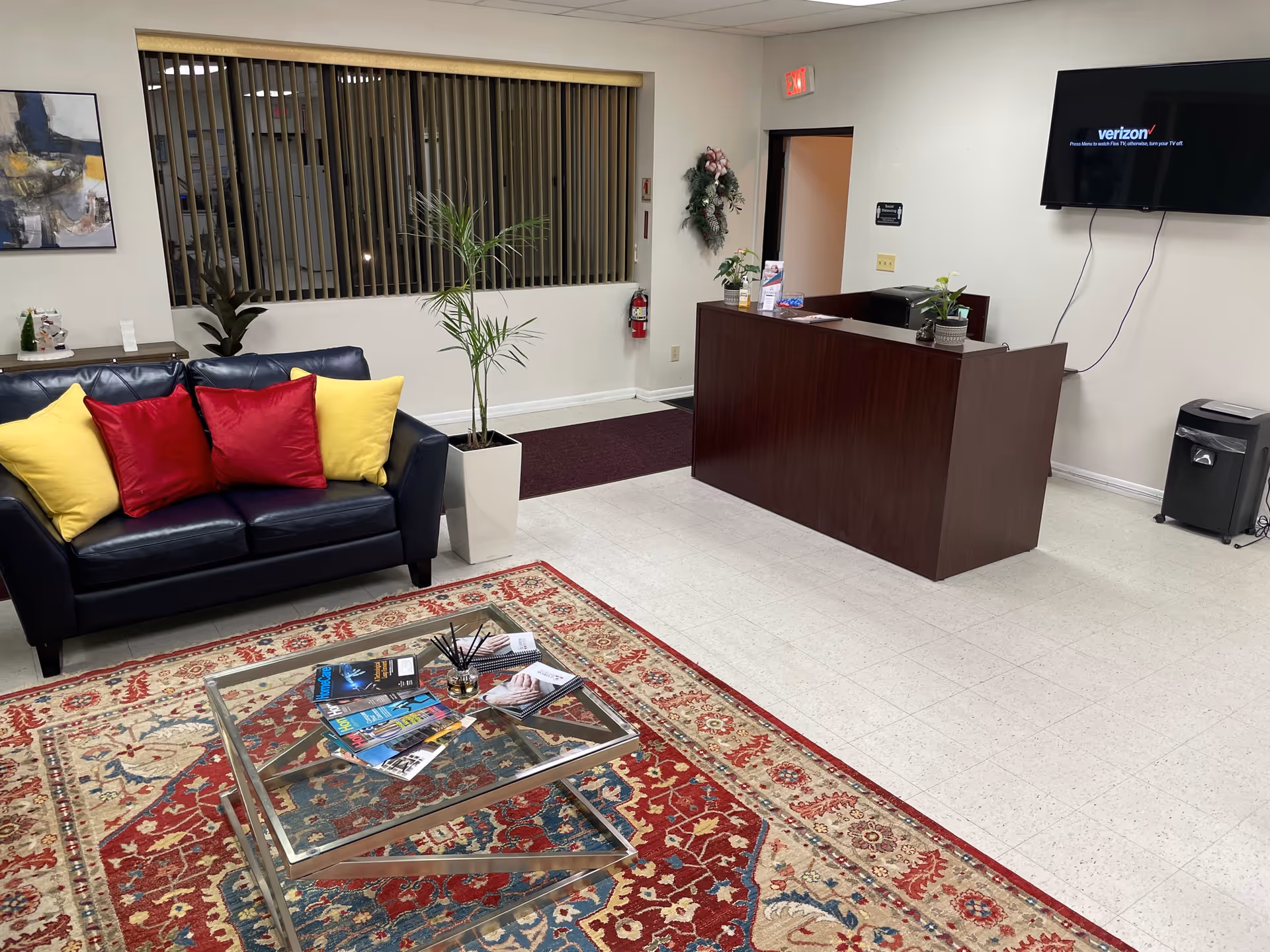 Interior in a senior living facility lobby: sofa seating, front desk, plants, magazines.