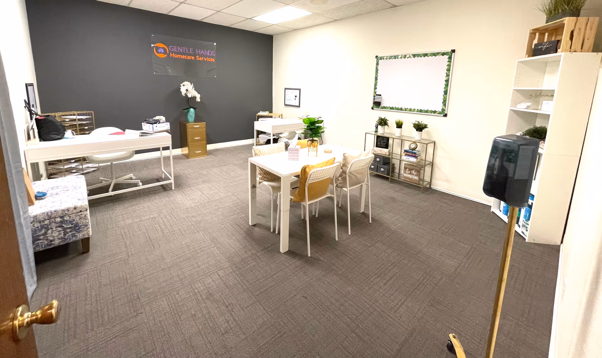 Bright interior common area with tables, chairs, plants, and a sign reading Gentle Hands Homecare Services.