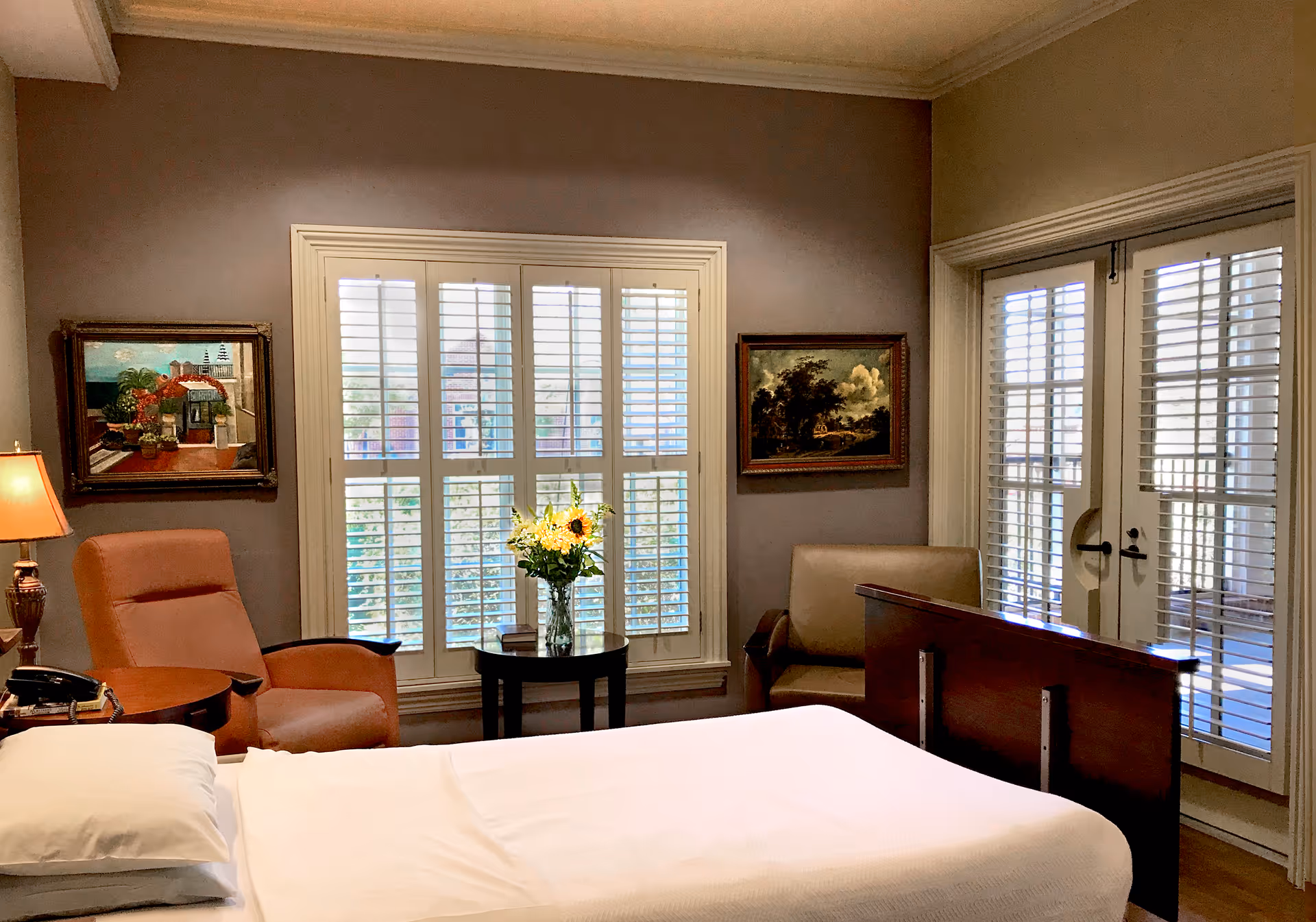 Bedroom in a hospice facility with a bed, chairs, and window shutters.