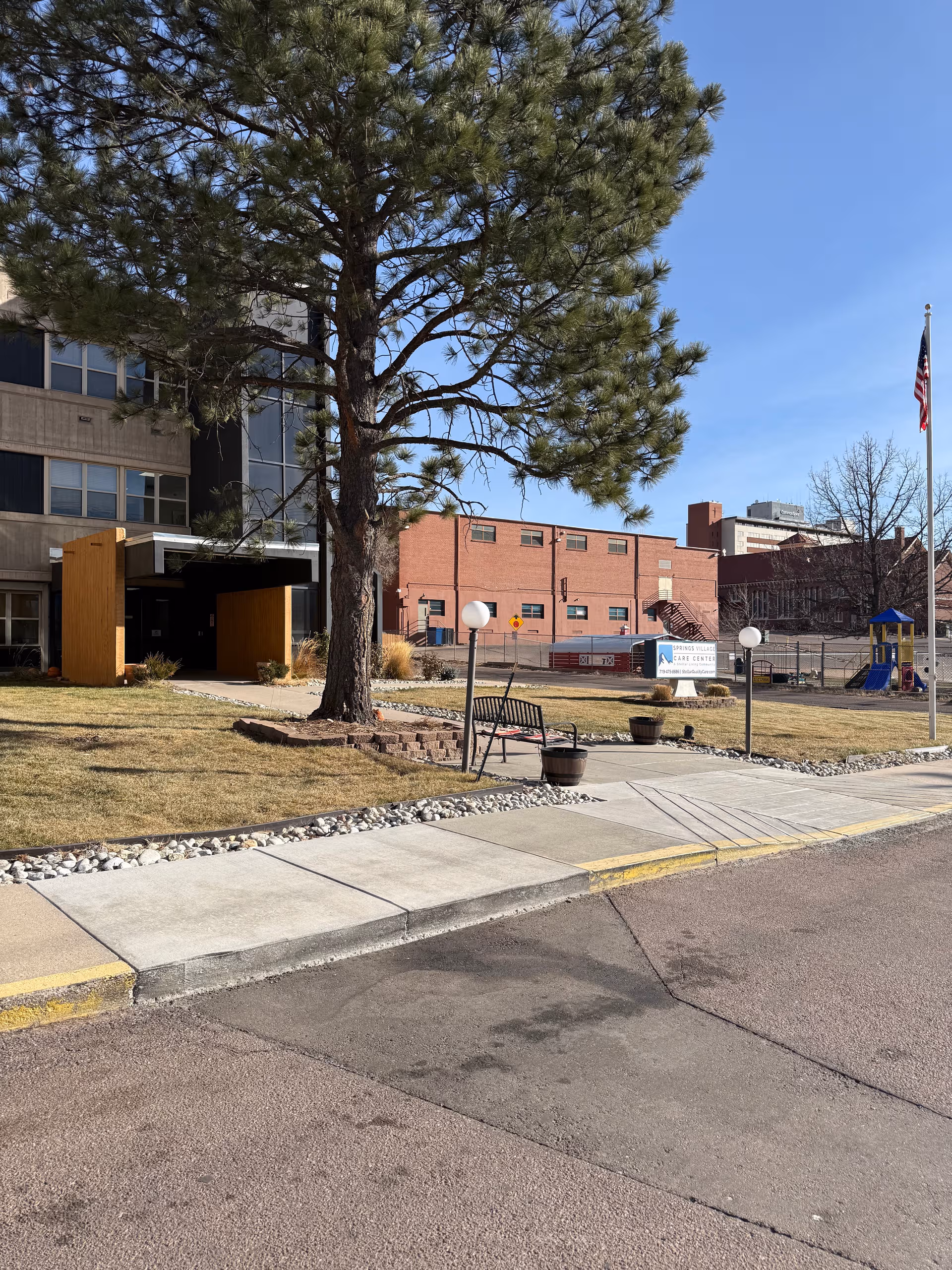 Exterior view of Springs Village Care Center with a large tree, sidewalk, and sign.