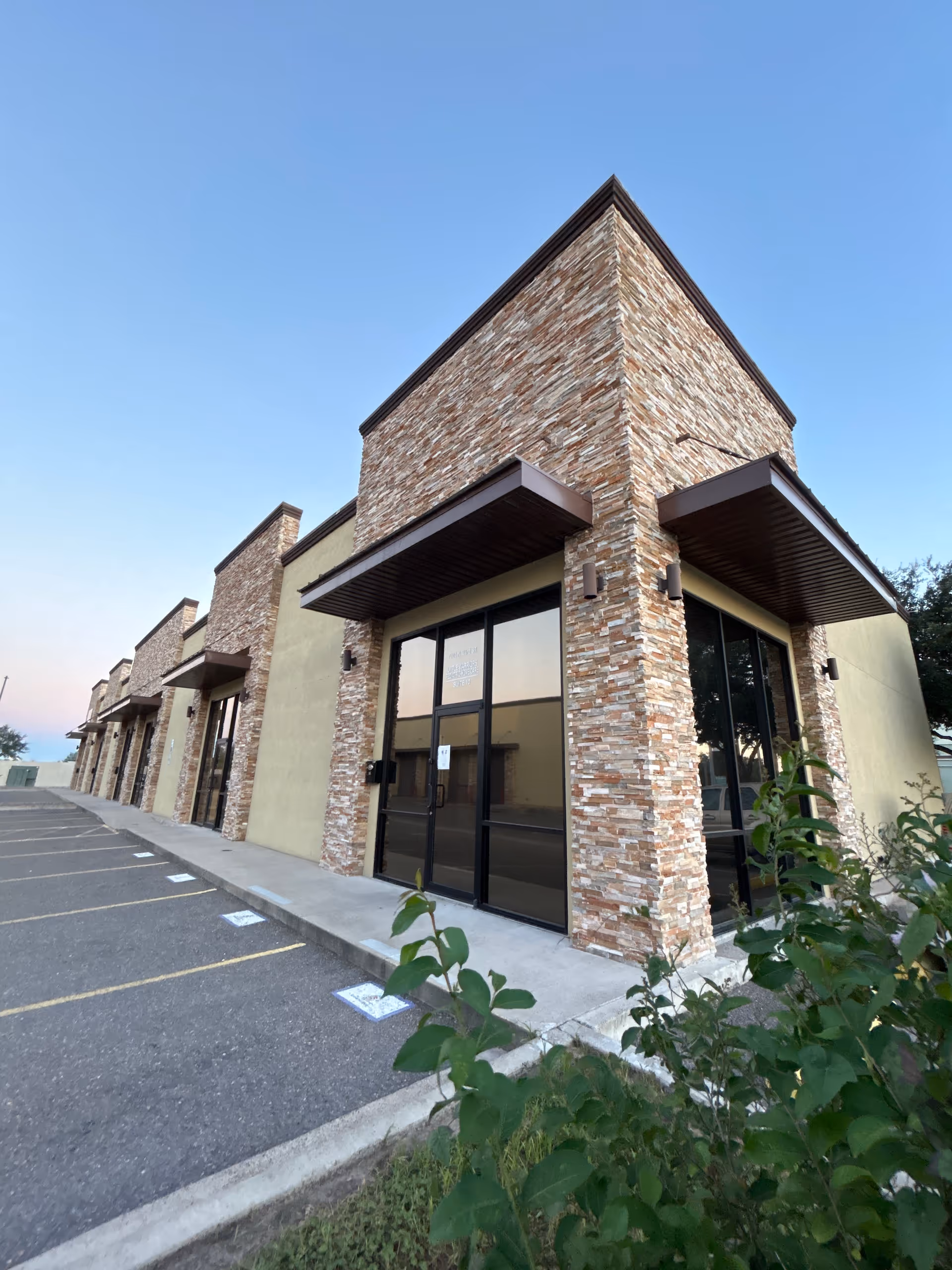 Stone-clad building exterior with glass entrance and adjacent parking lot.