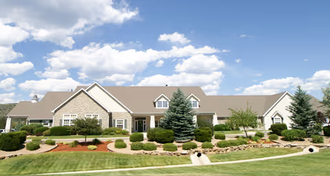 Single-story Brookdale Littleton building front with landscaped lawn, shrubs, and a blue sky with clouds.