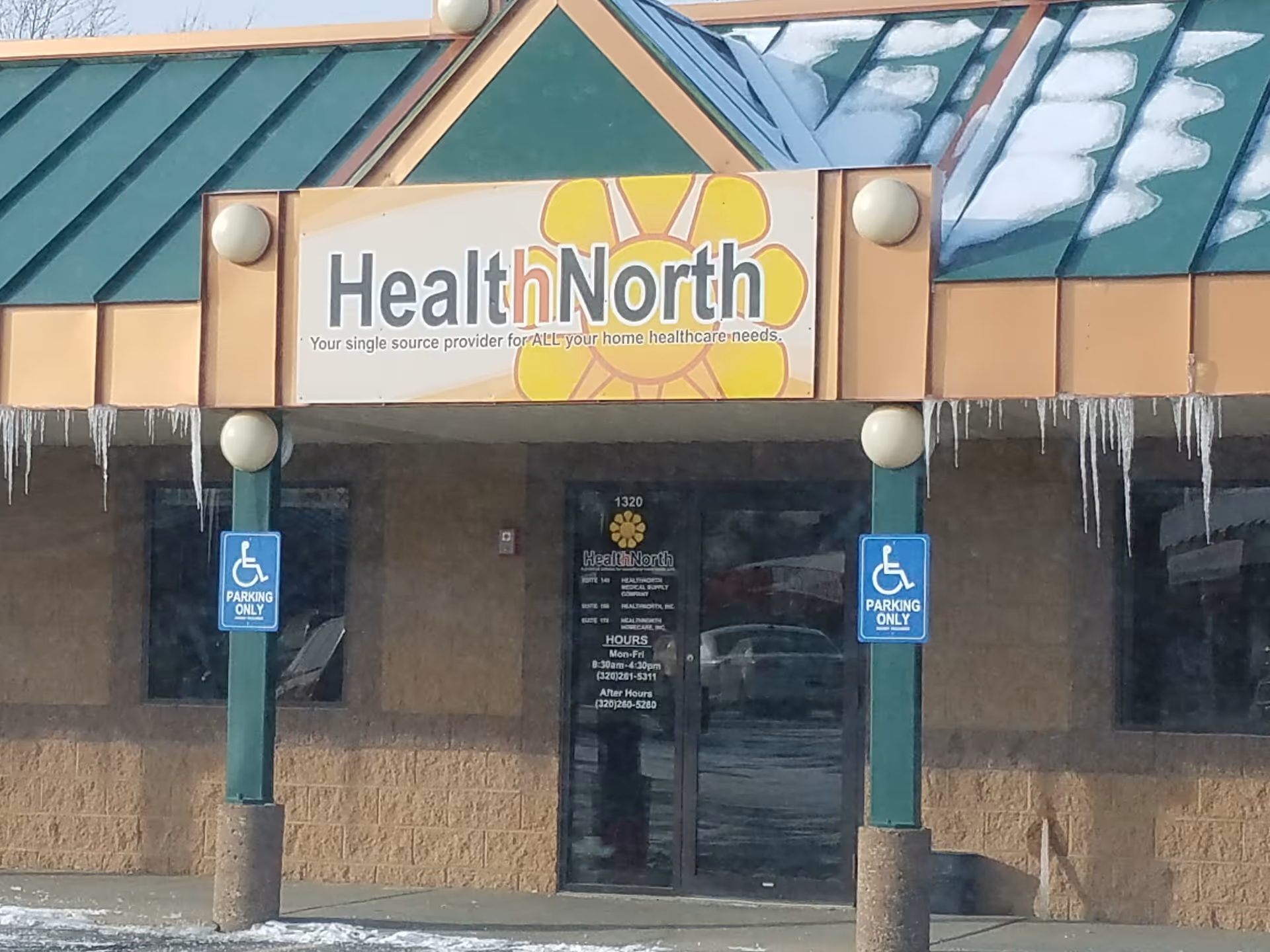 Exterior of HealthNorth facility entrance with sign, pillars, and handicap parking signs.