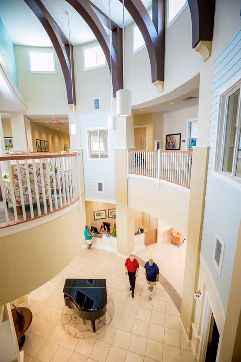 Atrium interior with a grand piano, curved dark arches, railings, and visitors.
