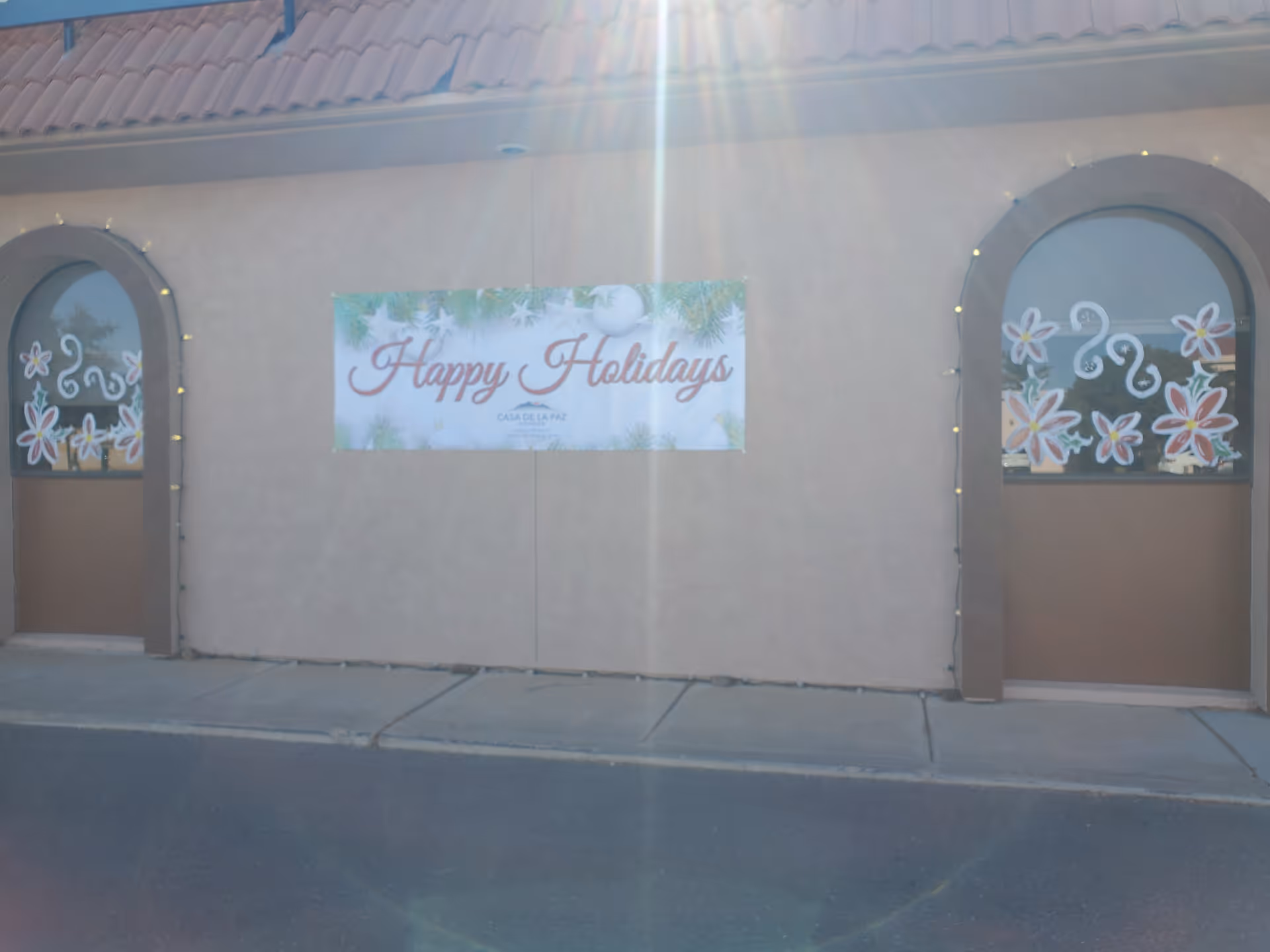 Exterior view of a beige building with a 'Happy Holidays' banner and arched windows.