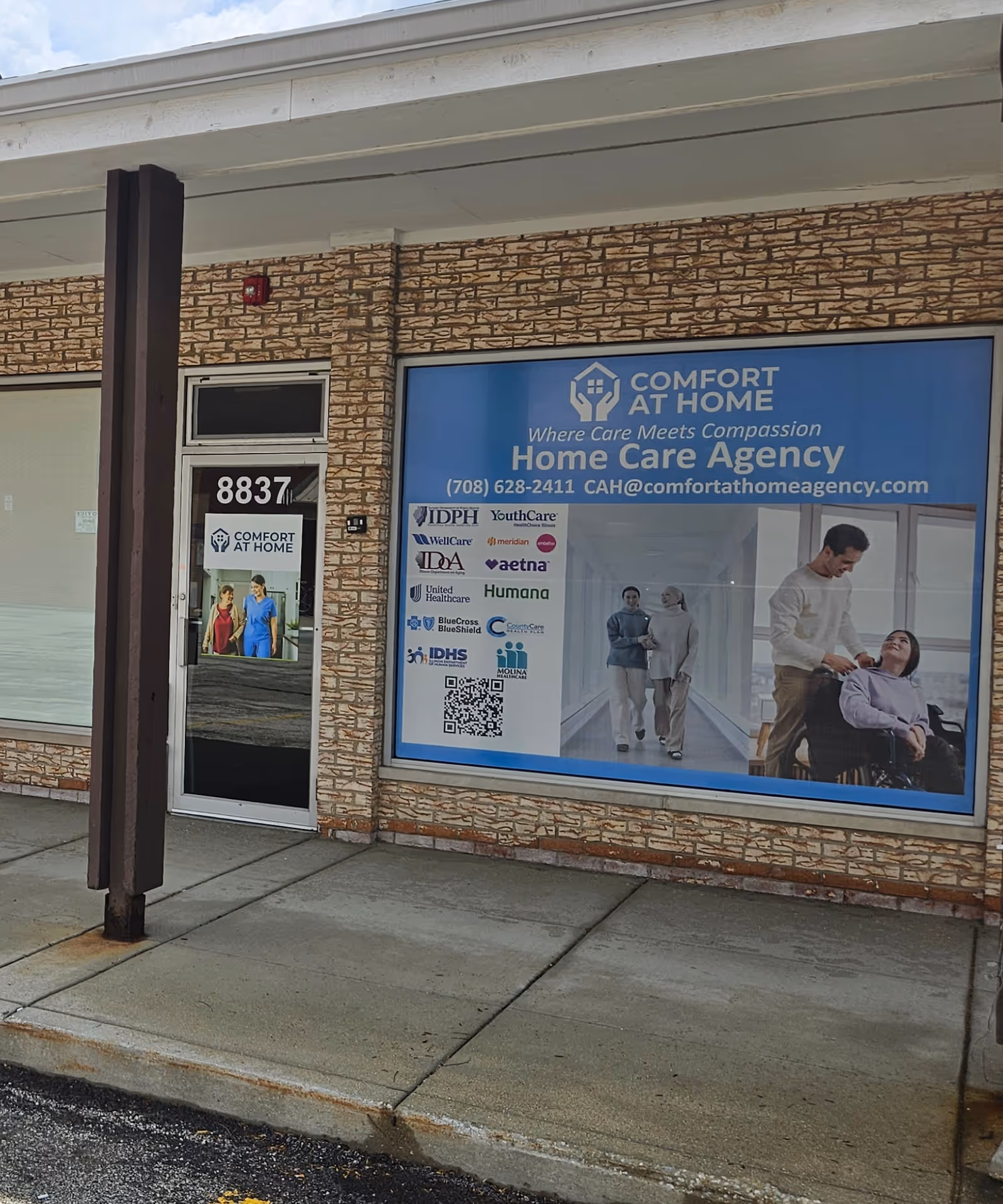 Exterior view of Comfort At Home storefront with large blue Home Care Agency sign.