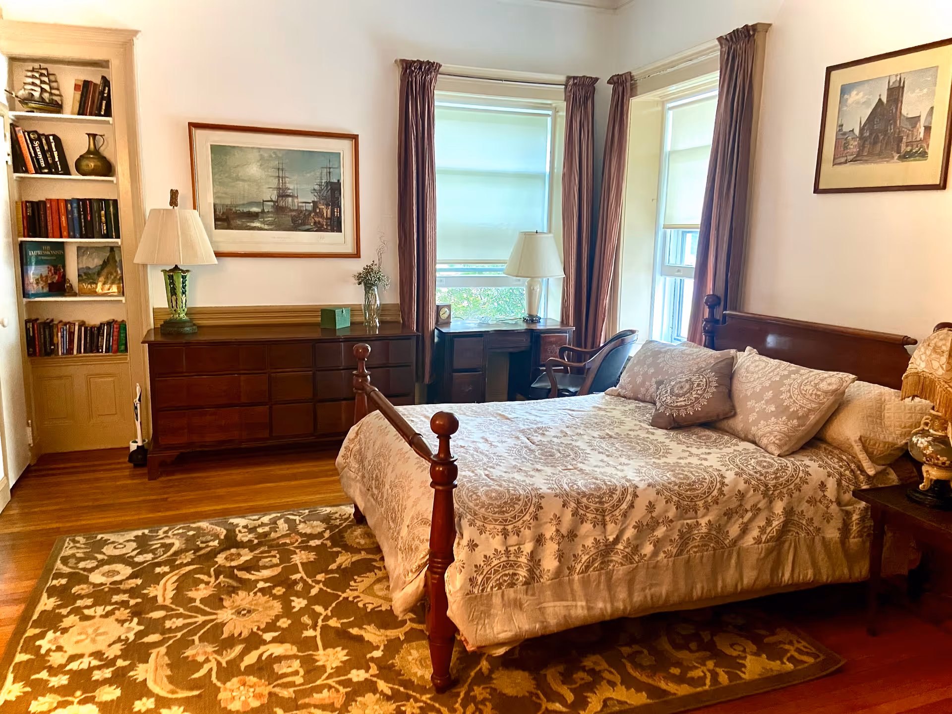 A cozy, well-furnished bedroom with a four-poster bed, dresser, desk, and bookshelf.