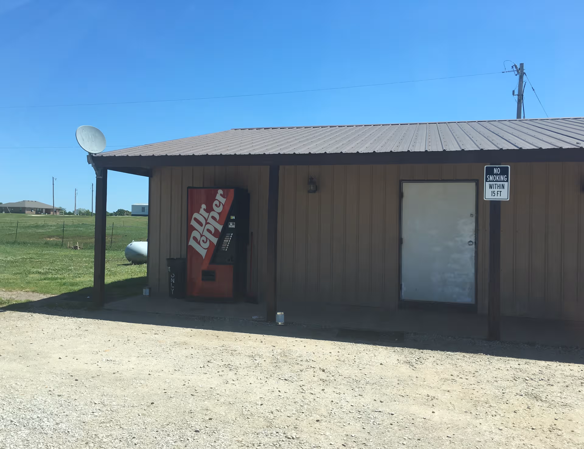 Small brown metal building with a Dr Pepper vending machine outside and a no-smoking sign.