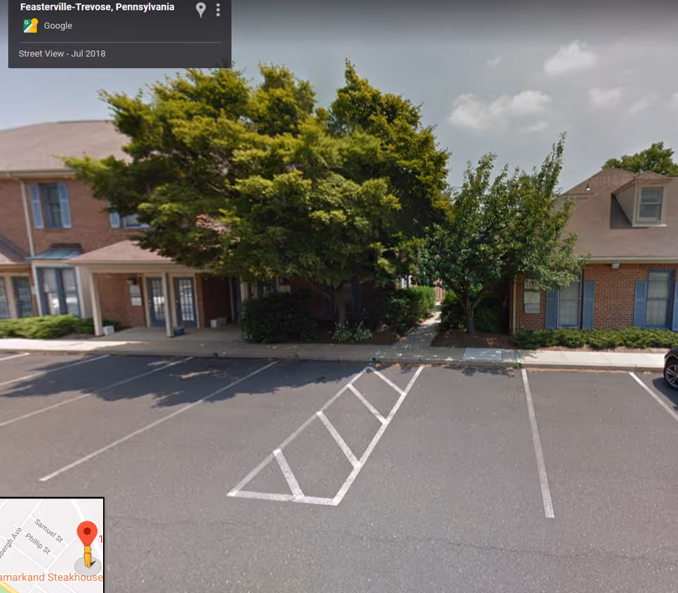 Exterior view of a brick senior living building with a tree-lined entrance and parking lot.