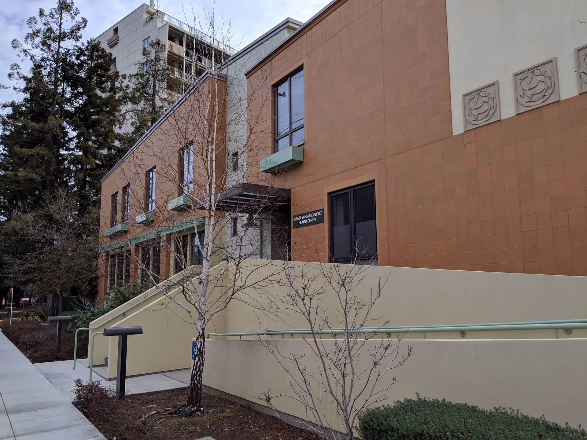 Exterior view of a brick senior living facility with ramp and bare trees.