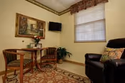 Cozy living room corner with round table, two chairs, black recliner, plant, and wall art.