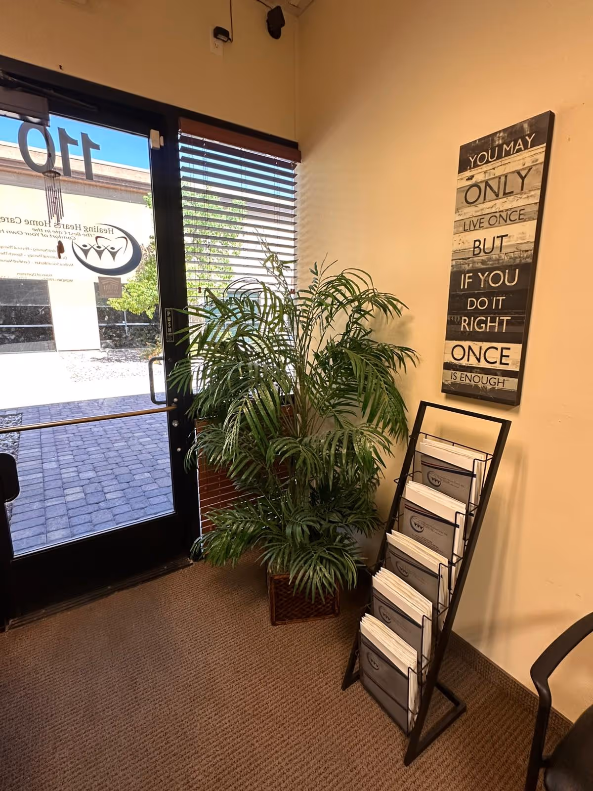 Lobby area near entrance with a potted palm plant, brochure rack, and wall decor.