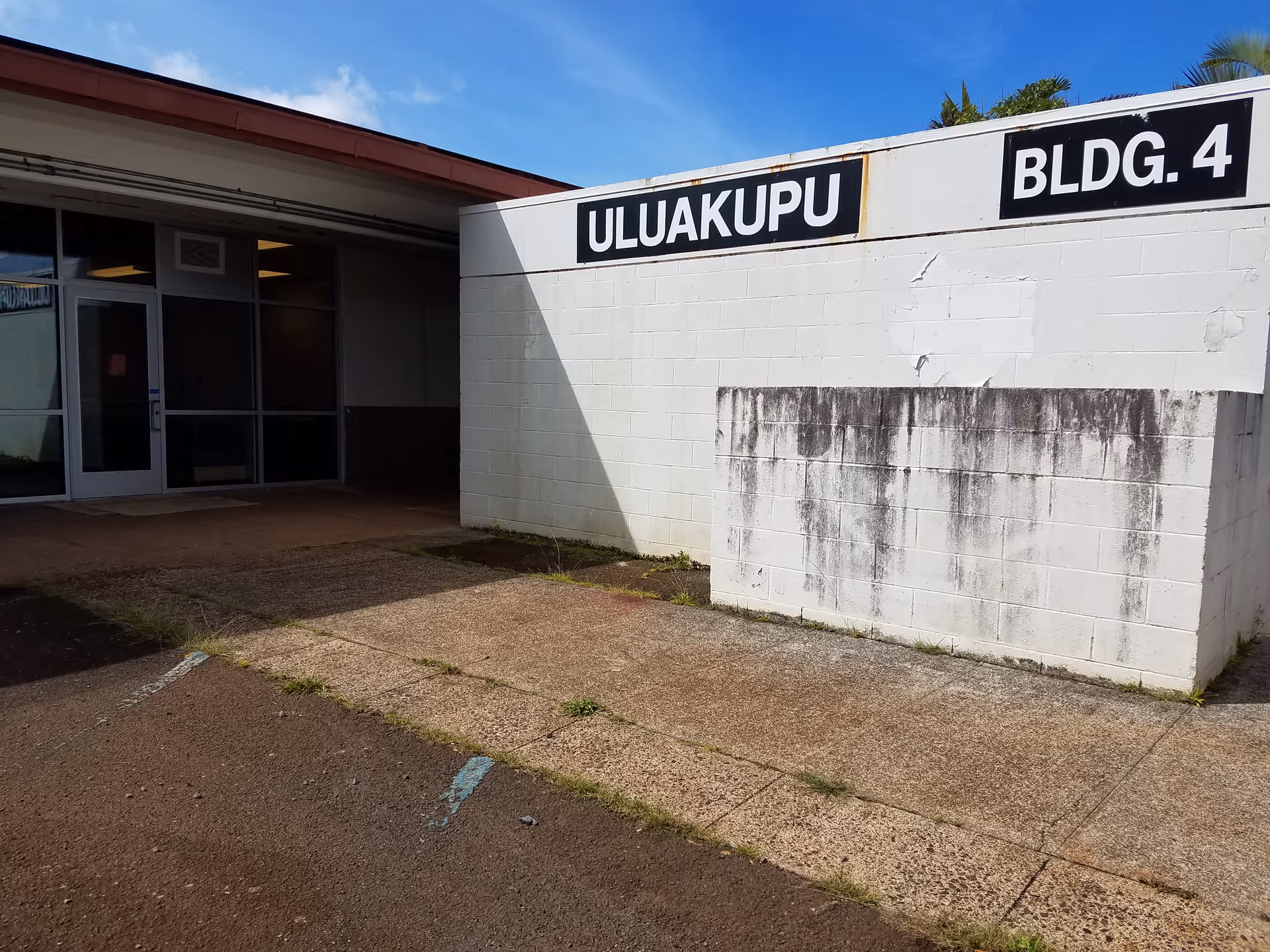 Exterior view of a white concrete building with a ULUAKUPU BLDG. 4 sign near an entrance.