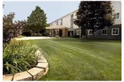 Front exterior of a senior living building with a green lawn and landscaped beds.