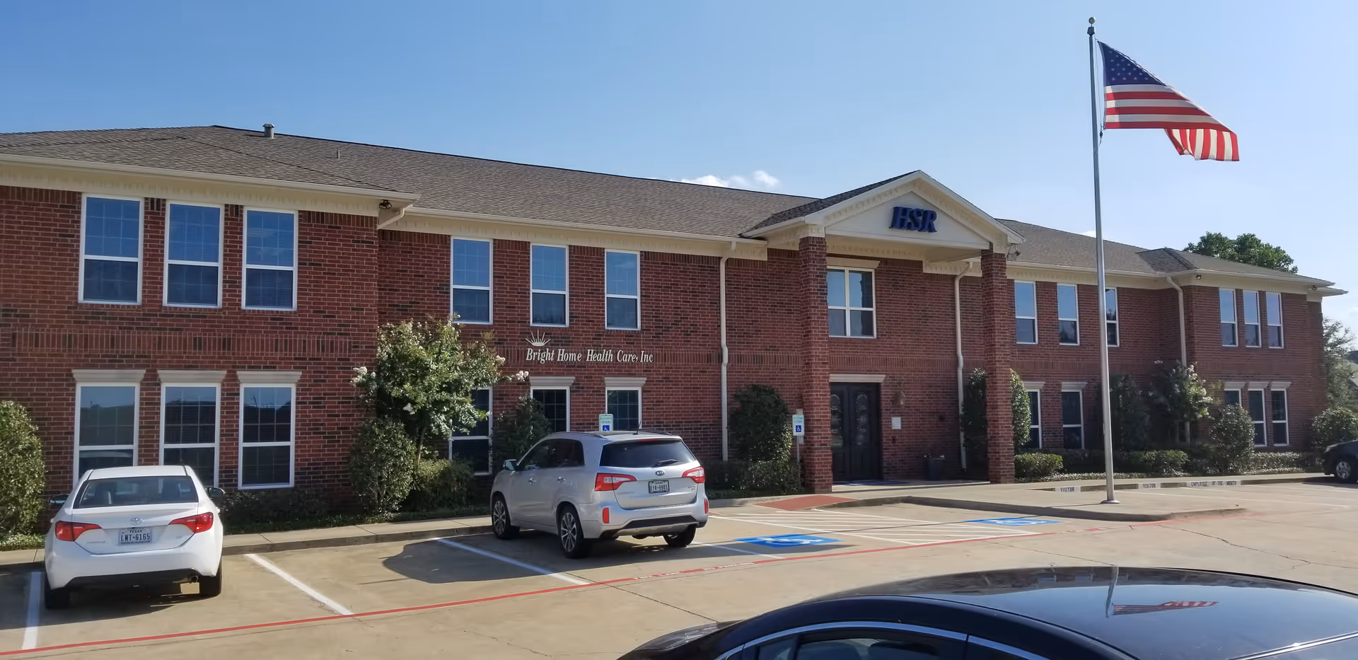 Brick Bright Home Health Care building facade with parked cars and an American flag in front.