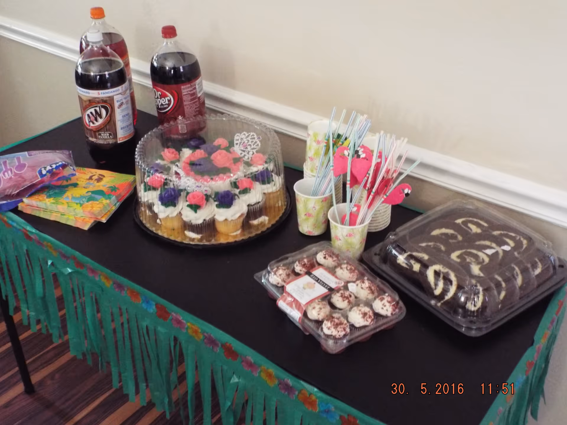 Party table with cupcakes, dessert trays, soda bottles, and cups with straws.