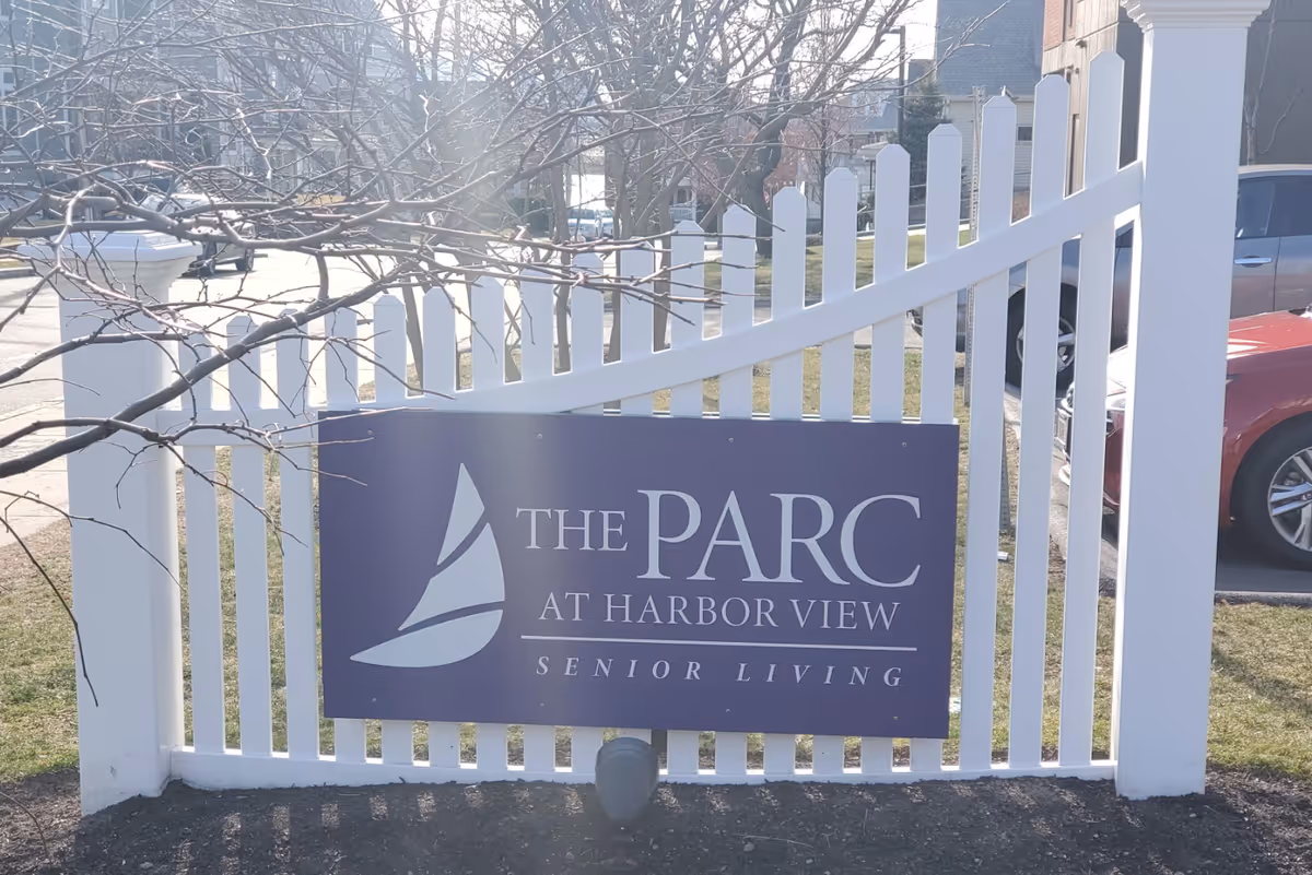 White picket fence with a purple sign for The Parc at Harbor View Senior Living.
