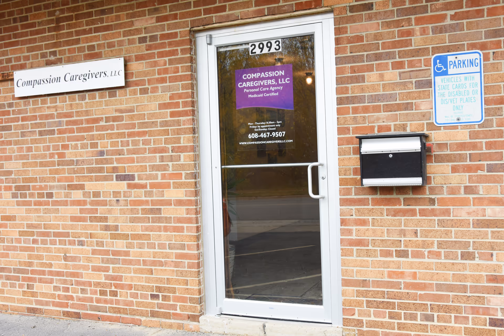Brick exterior entrance with Compassion Caregivers LLC sign and parking sign.