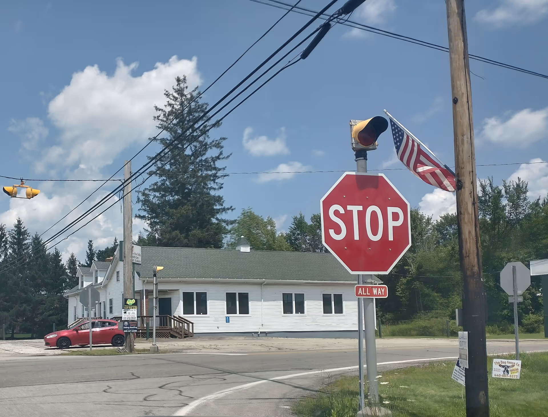 Street view of a white, single-story building with a stop sign and American flag.