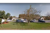 Parking lot with cars, grassy area, and trees in front of a facility.