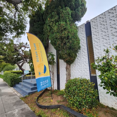Exterior view of facility entrance with blue steps, greenery, and a yellow banner sign