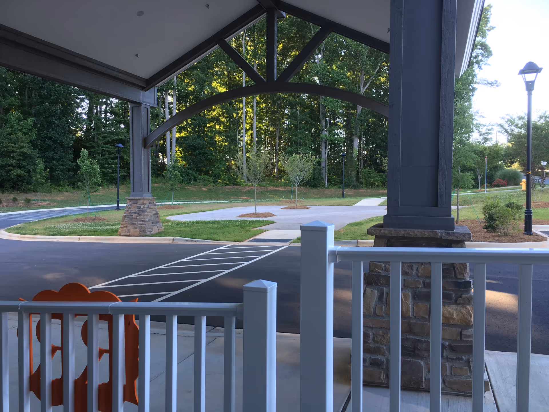 Covered entrance with arched framework and stone pillars over a parking lot.