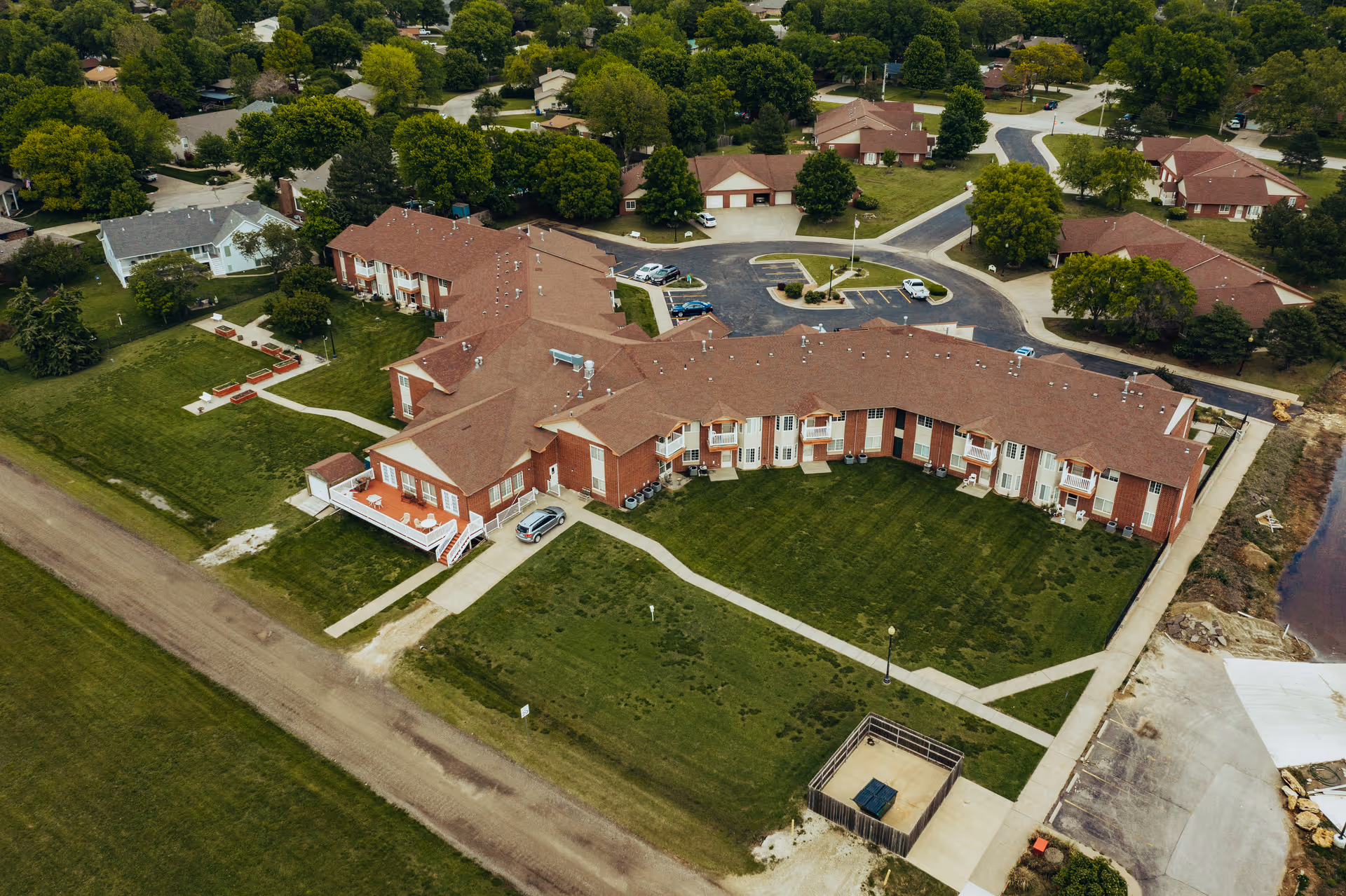 Aerial view of Cottonwood Point senior living complex showing curved brick buildings with red roofs, lawns, walkways, and nearby homes and parking areas.