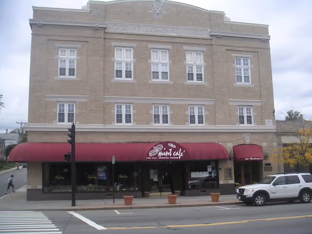 Brick building with red canopy Mint Cafe storefront and parked white SUV.