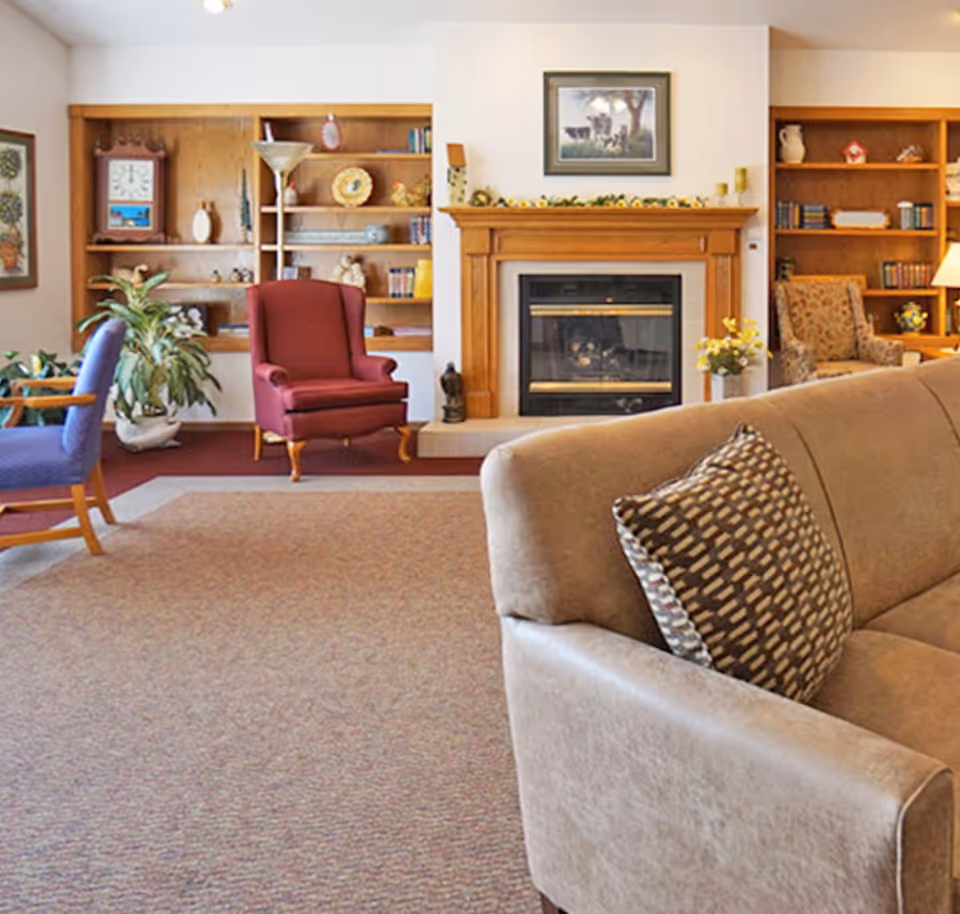 Cozy seating area with a sofa and armchairs facing a wood-framed fireplace flanked by built-in bookshelves.