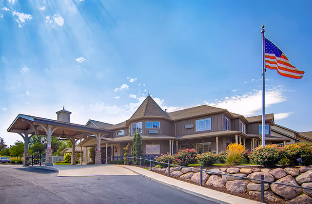 Exterior view of Rocky Mountain Care Grove Creek Assisted Living facility with flag, entrance, and landscaping.
