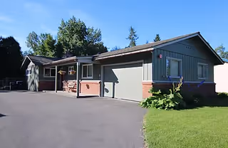 Single-story senior living building with a driveway, attached garage, and front lawn under a blue sky.