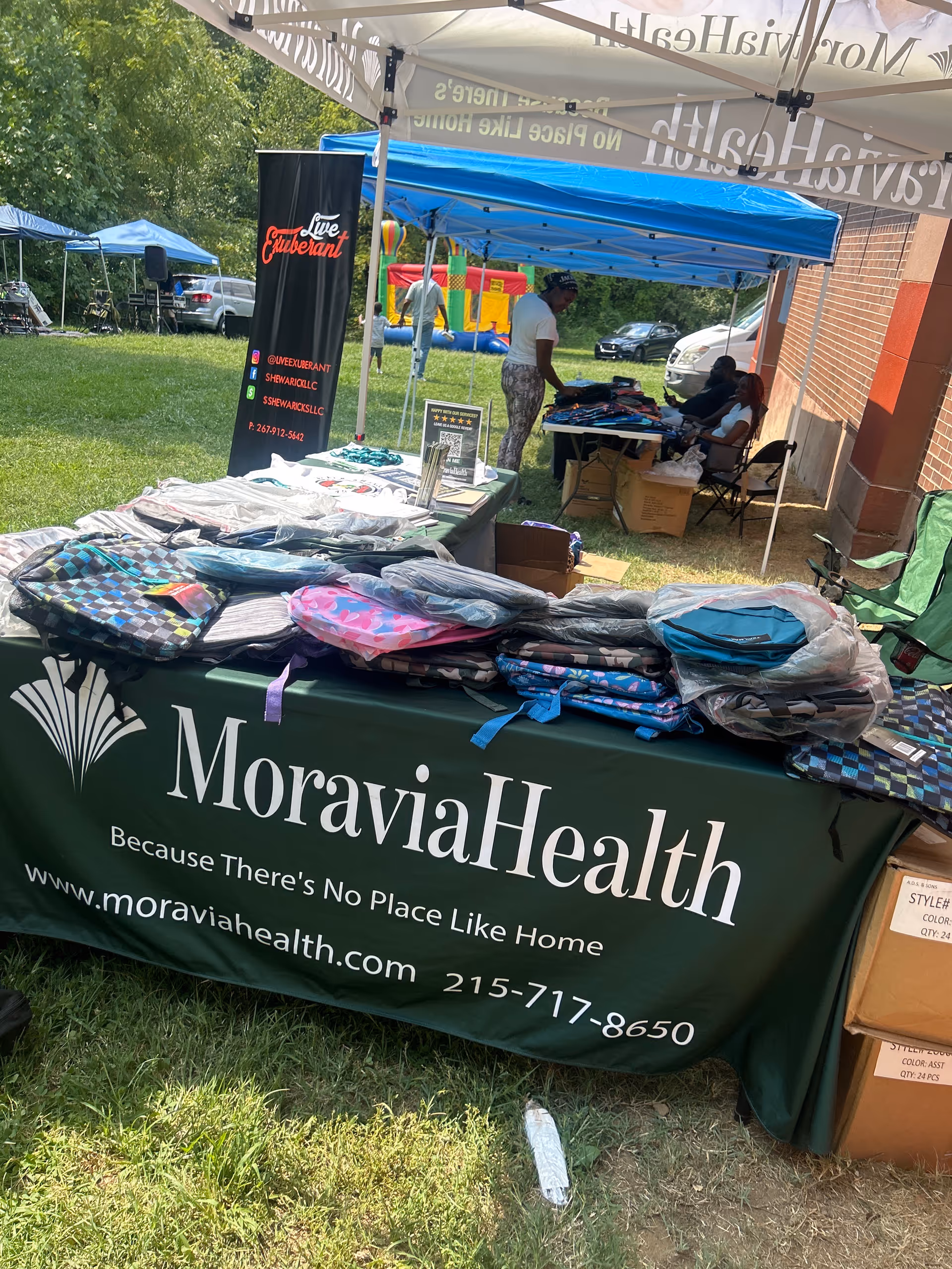 Outdoor MoraviaHealth booth with tents, tables, and branded merchandise.