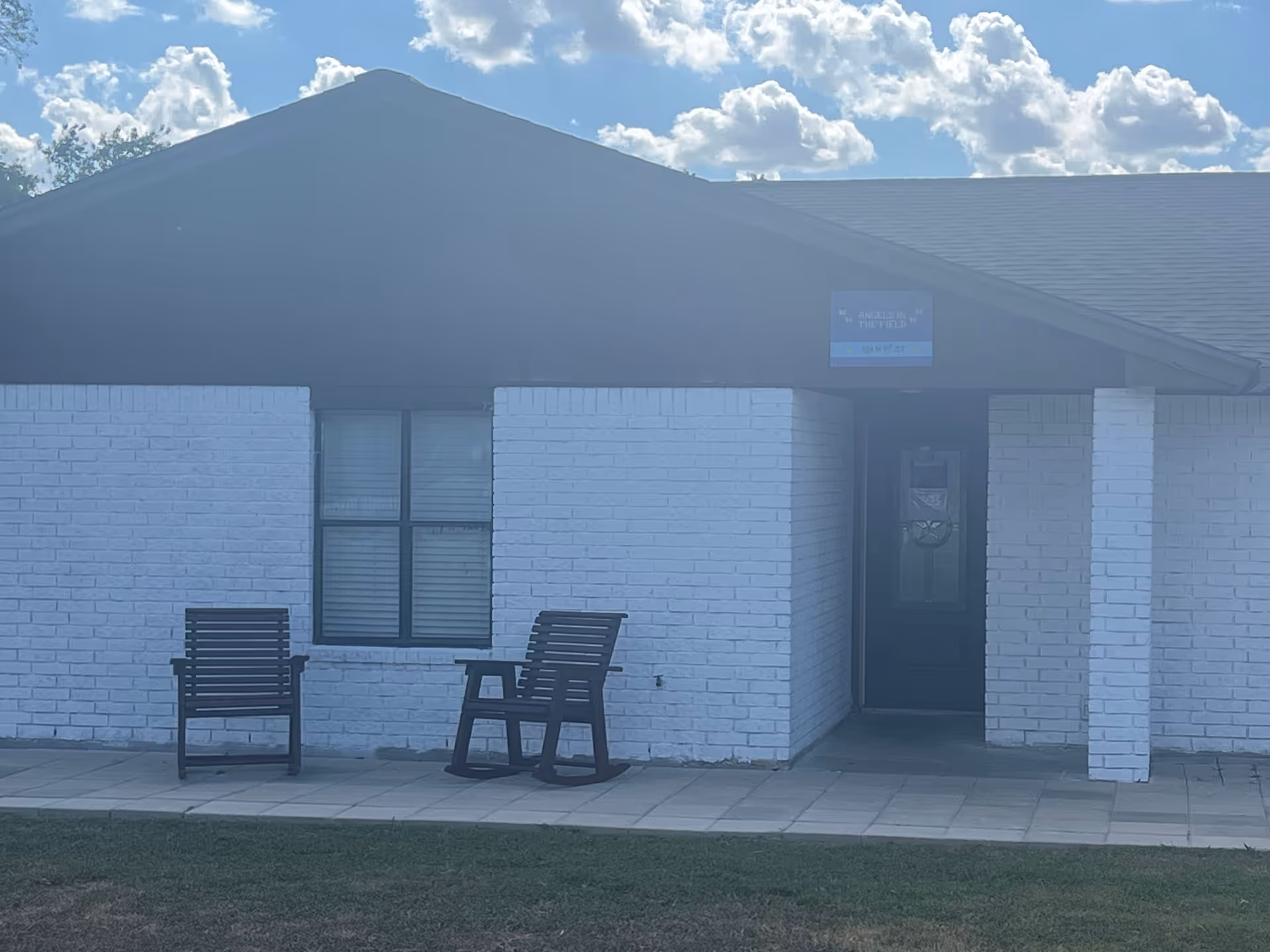 Exterior of a white brick senior facility with two rocking chairs.