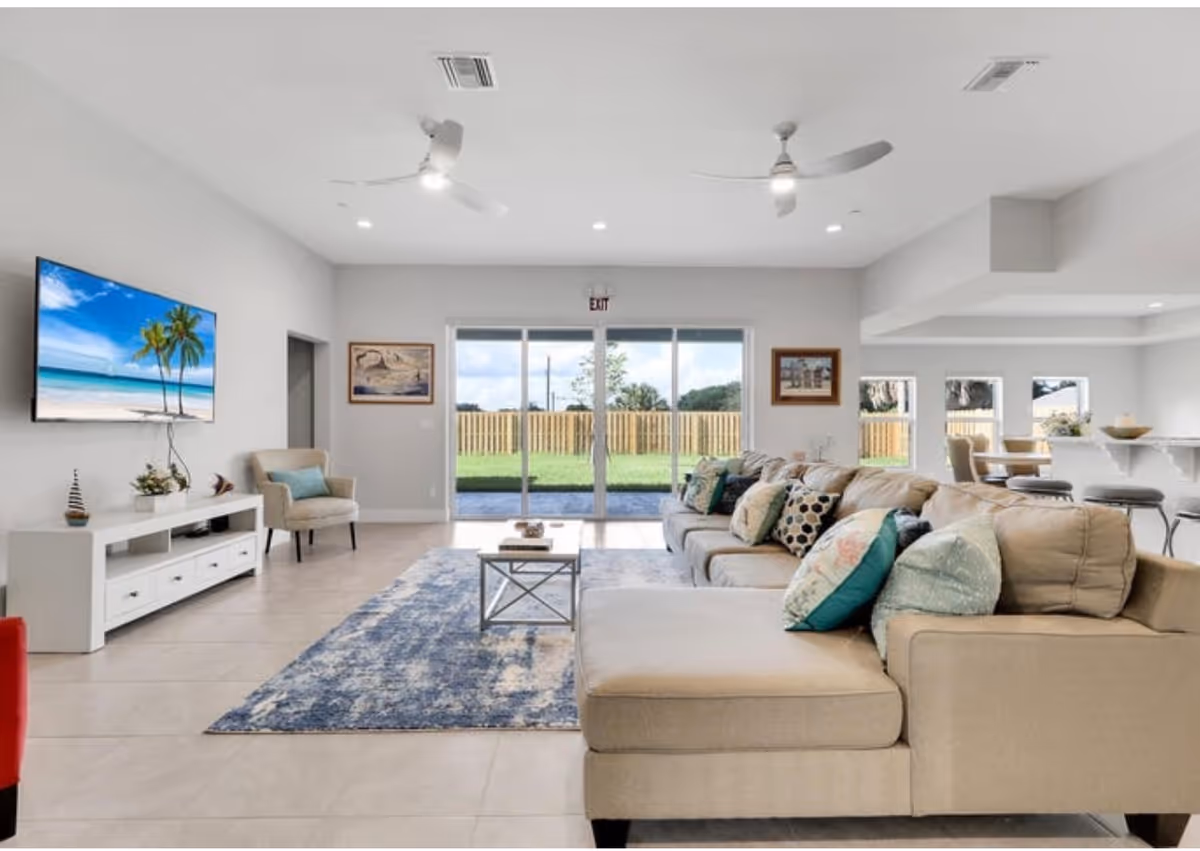 Bright living room with beige sectional, rug, TV, and sliding glass doors to a fenced yard