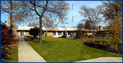 Front view of Woodlands at Hampton Woods showing lawn, trees, and sidewalk.
