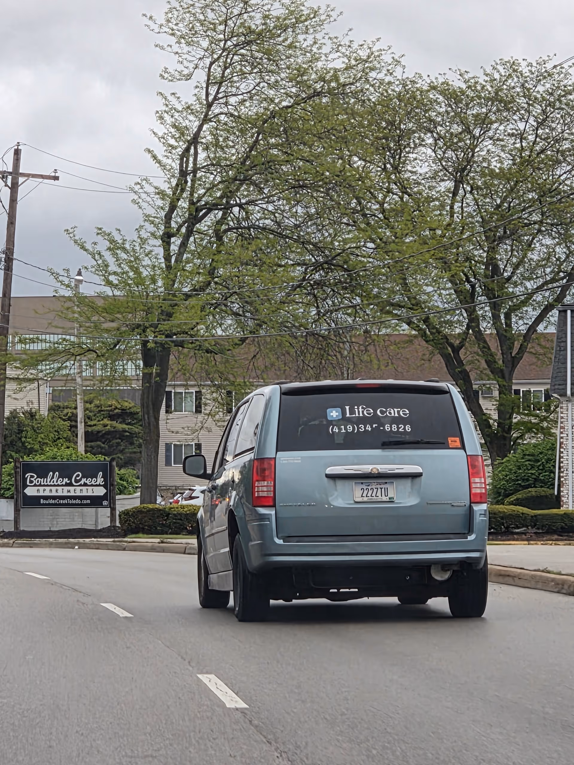 Blue Life Care van on a street near an apartment complex sign.
