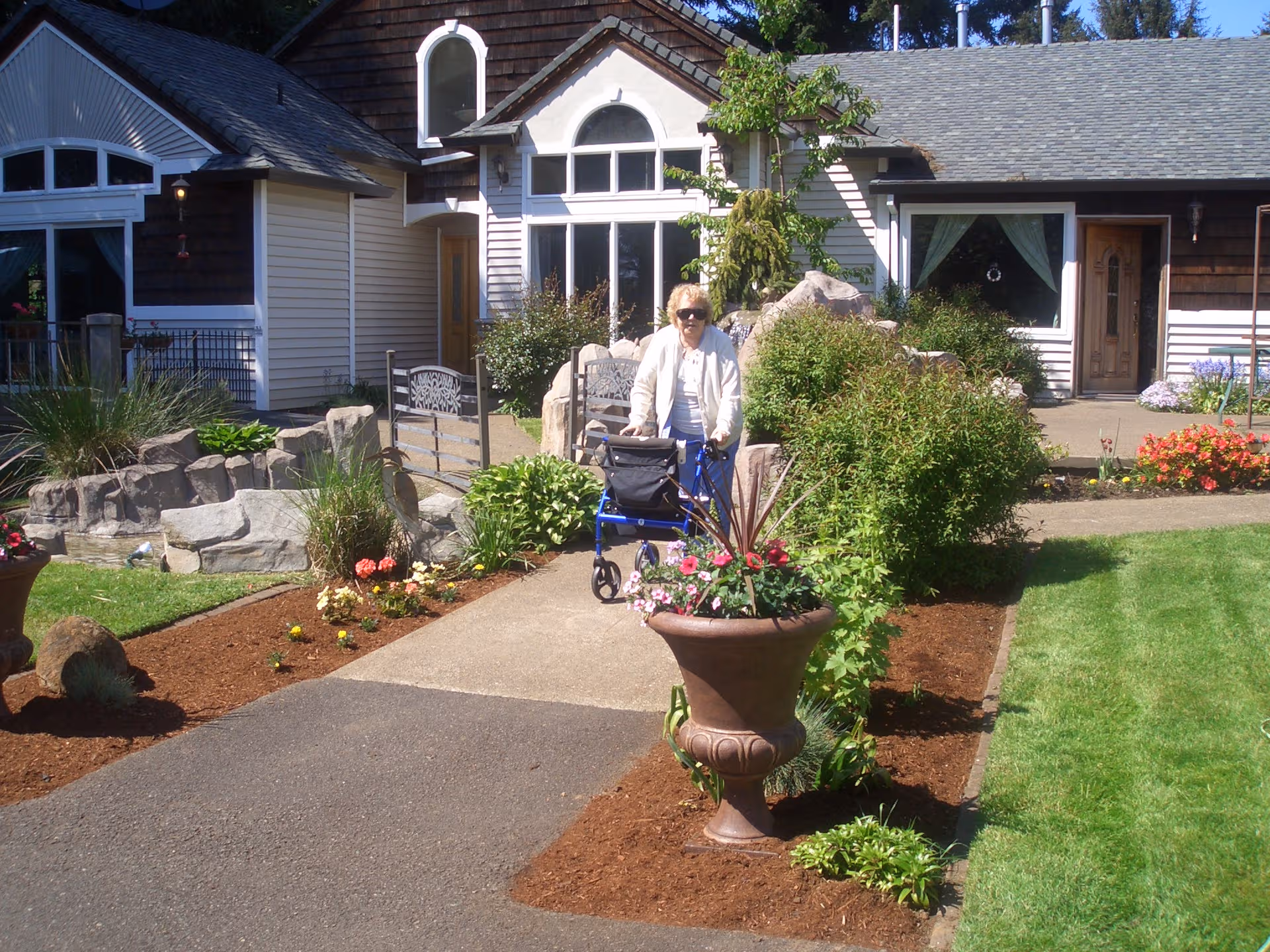 Senior woman with a walker on a landscaped path in front of RiverCrest Senior Living.