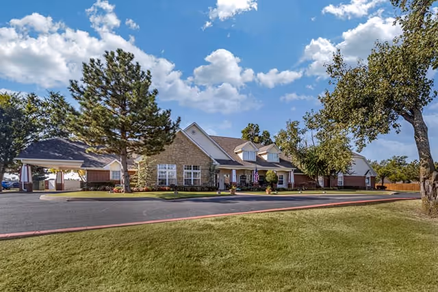 Front exterior view of a brick senior living facility with trees and a parking lot.