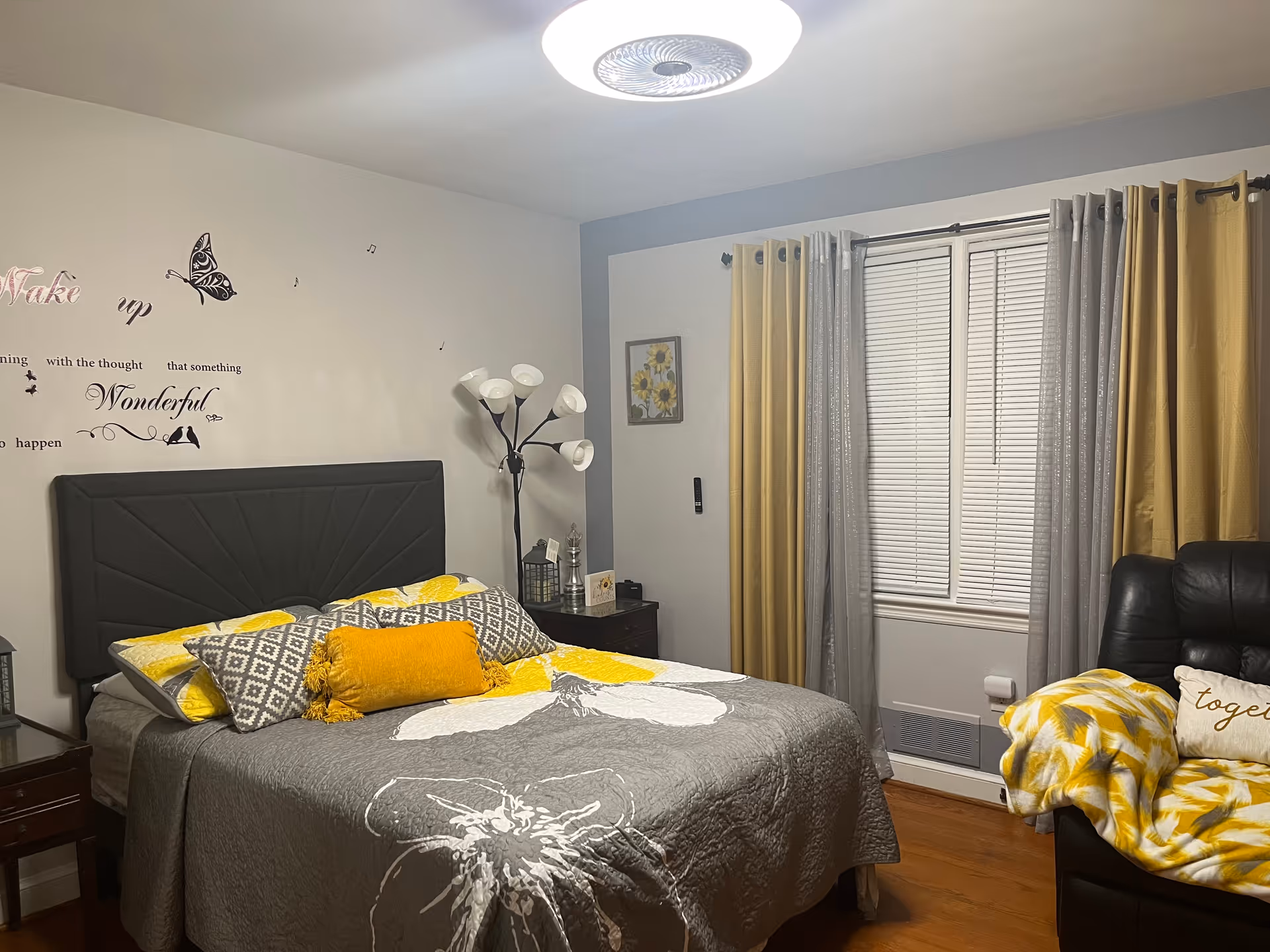 A decorated bedroom with a bed, pillows, nightstands, and a window with yellow and gray curtains.