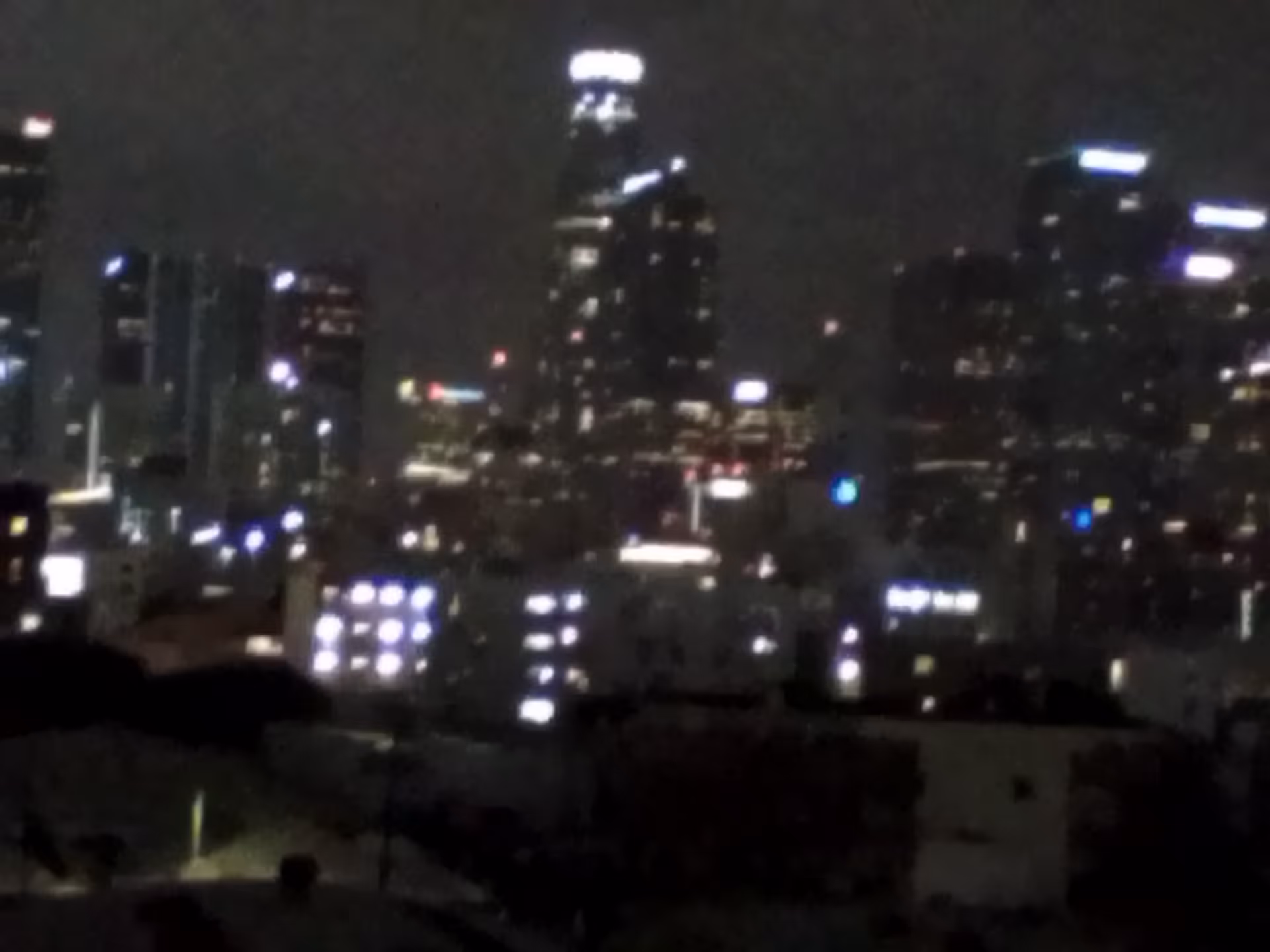 Nighttime city skyline with illuminated high-rises and a dark foreground.