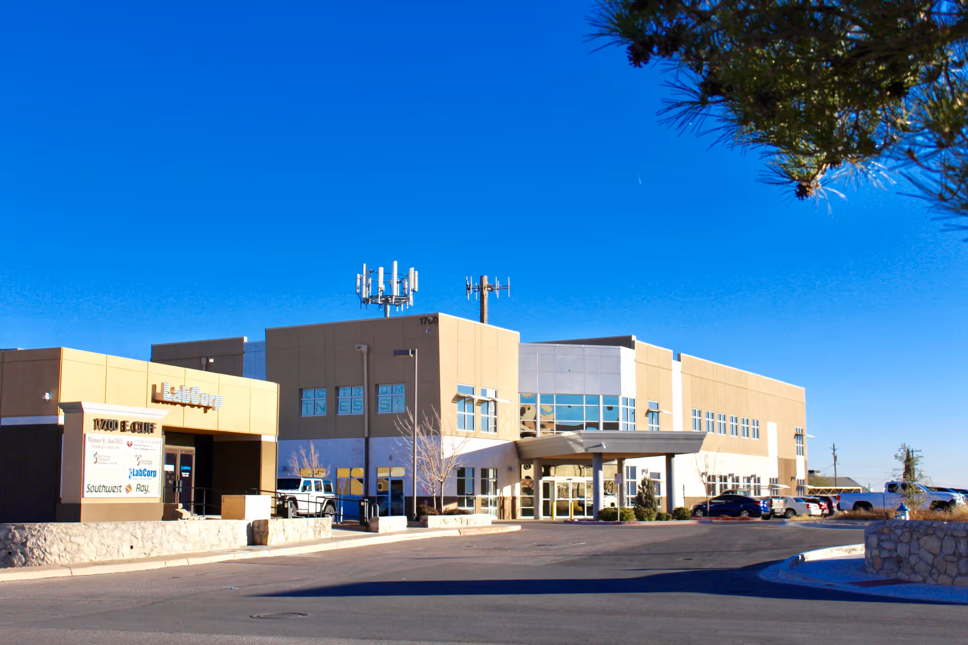 Exterior view of a modern beige medical facility with a glass entrance and parking lot.