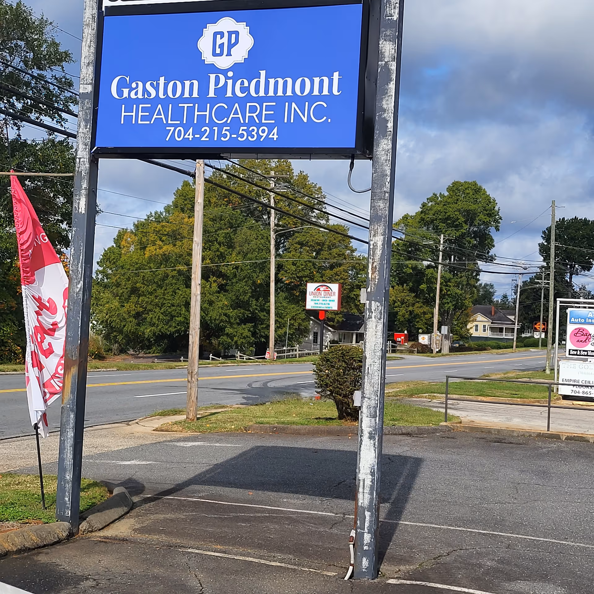Large blue Gaston Piedmont Healthcare sign on a tall weathered frame beside the road.