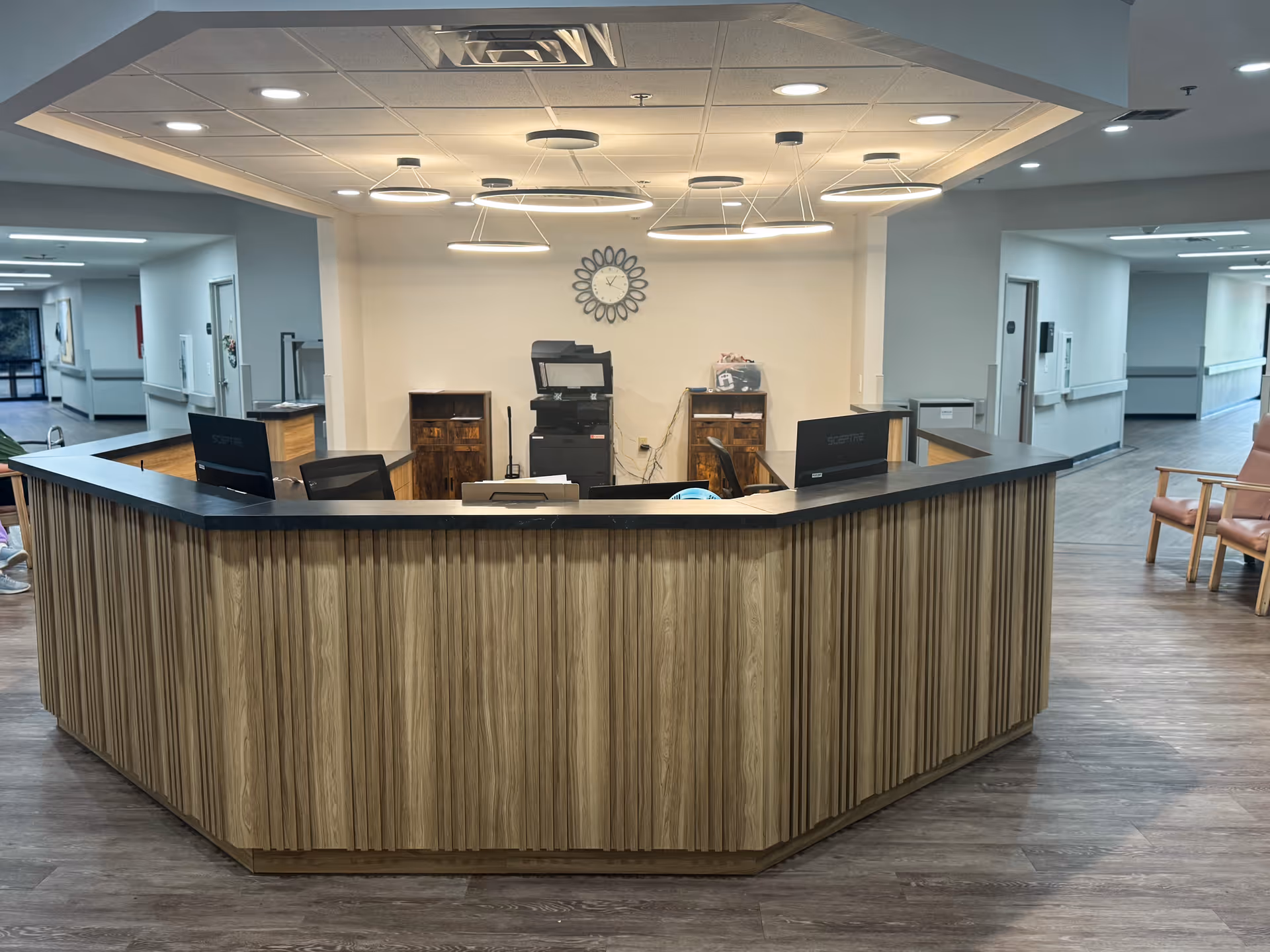 Curved wooden reception desk in a bright senior living facility lobby with hallways.