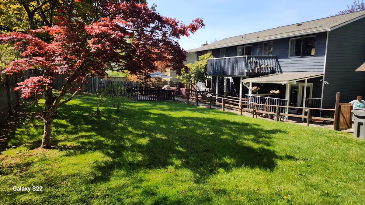 Two-story senior living home with a spacious grassy yard, deck, and wooden fence.