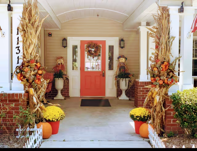 Front entrance with a pink door, fall wreath, cornstalks, and pumpkins.