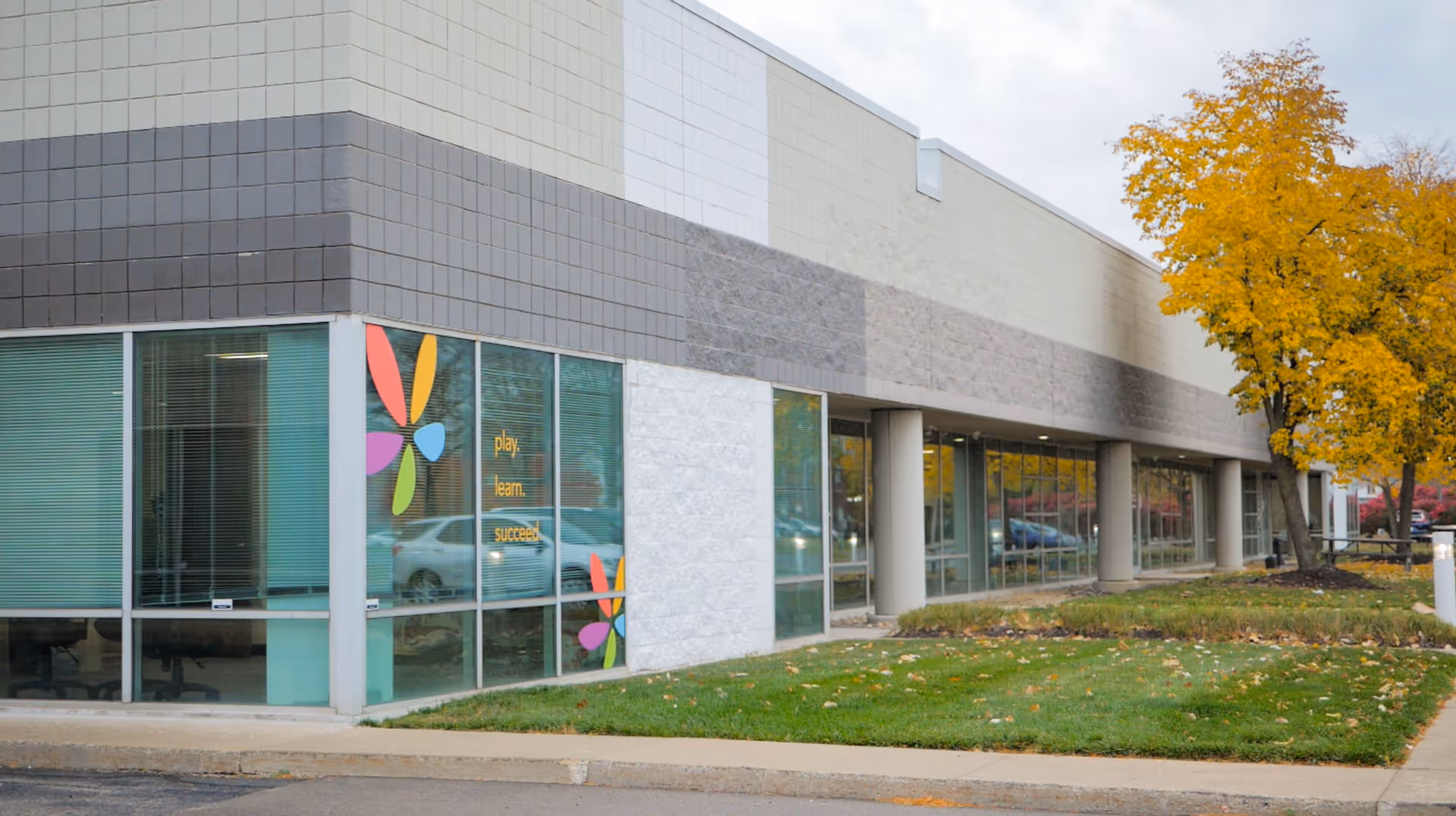 Modern commercial building exterior with glass windows and autumn trees nearby.