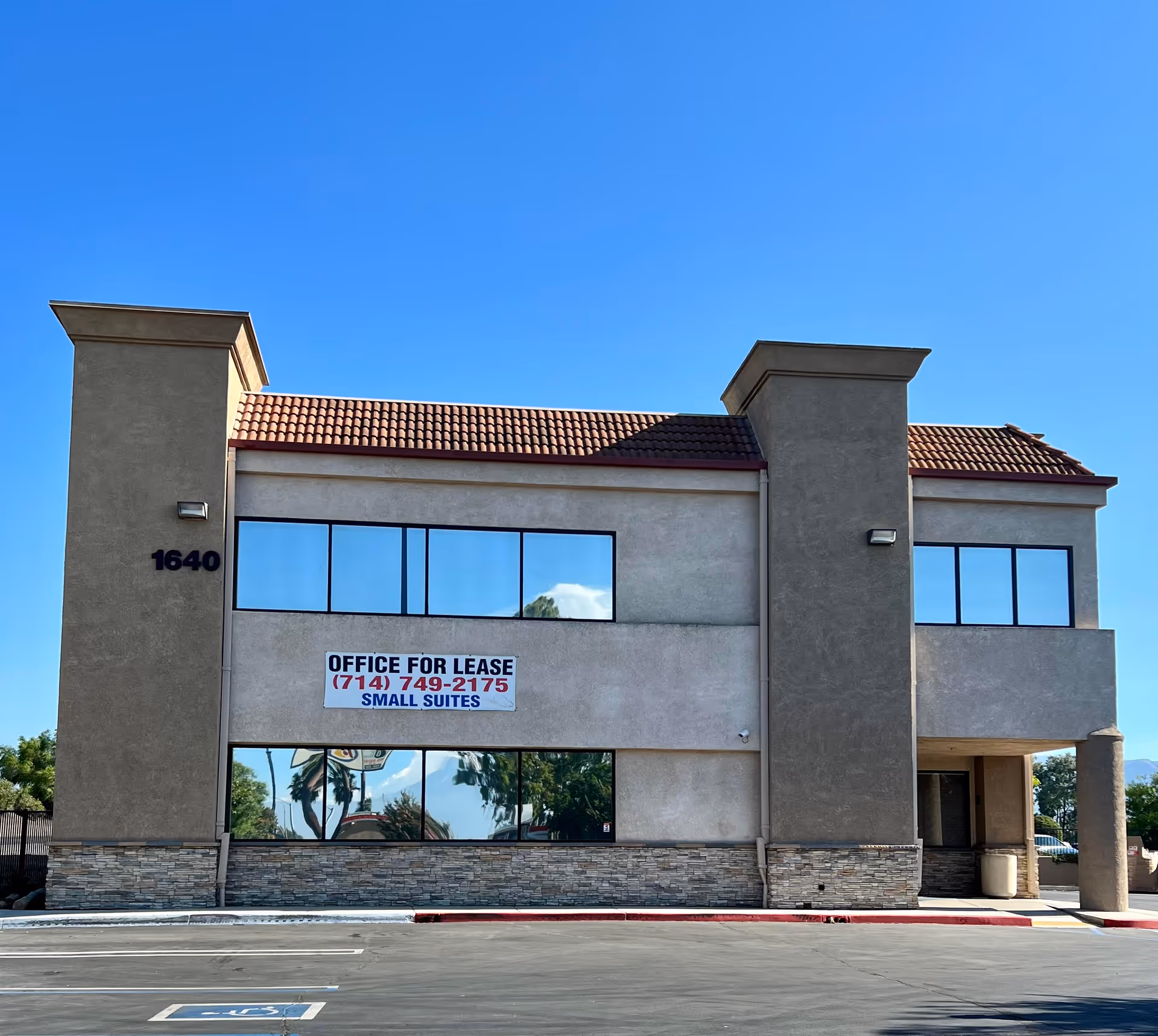 Two-story beige building with large front windows, red-tiled roof, and an 'Office for Lease' banner.